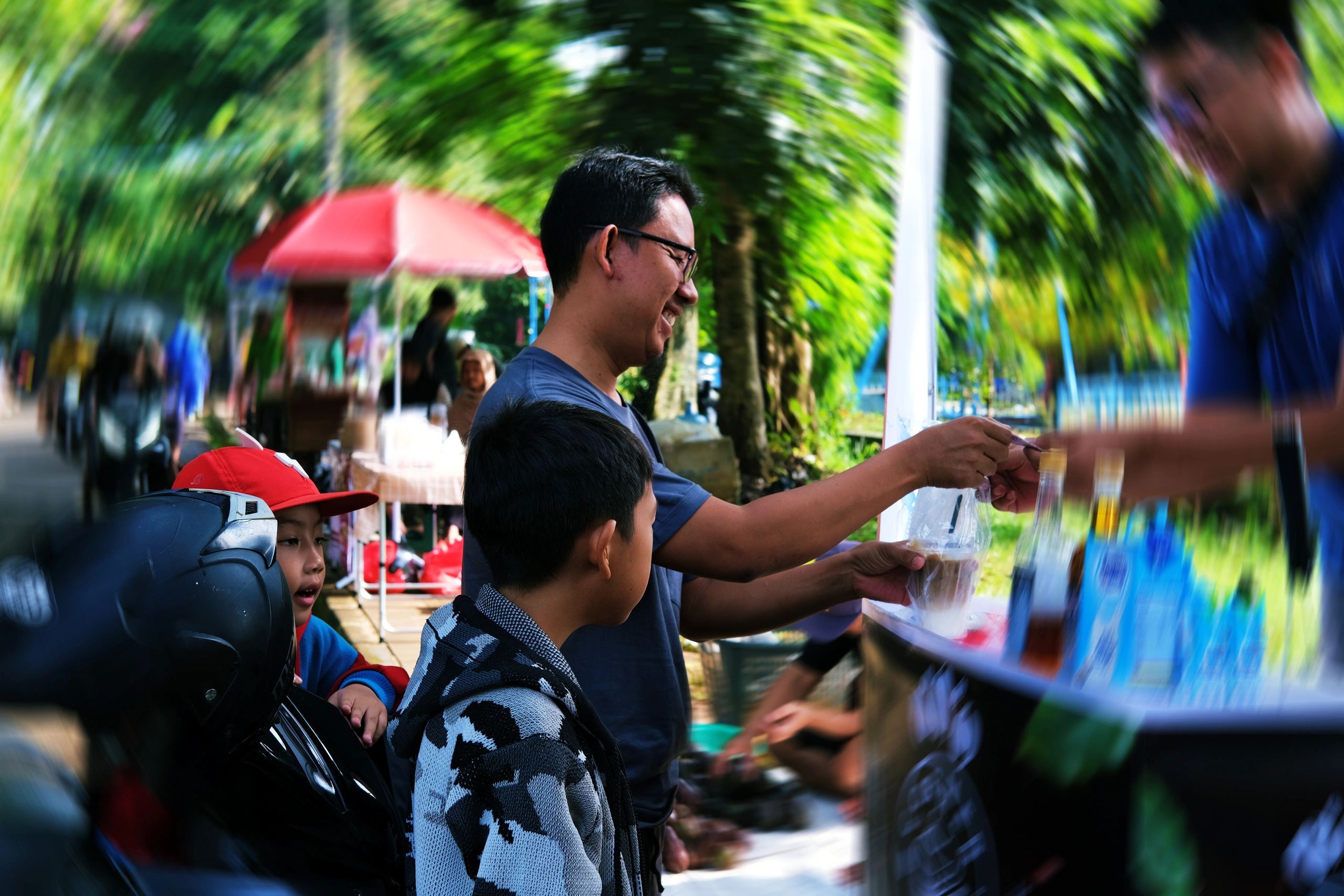 Outdoor market stall with shoppers and greenery