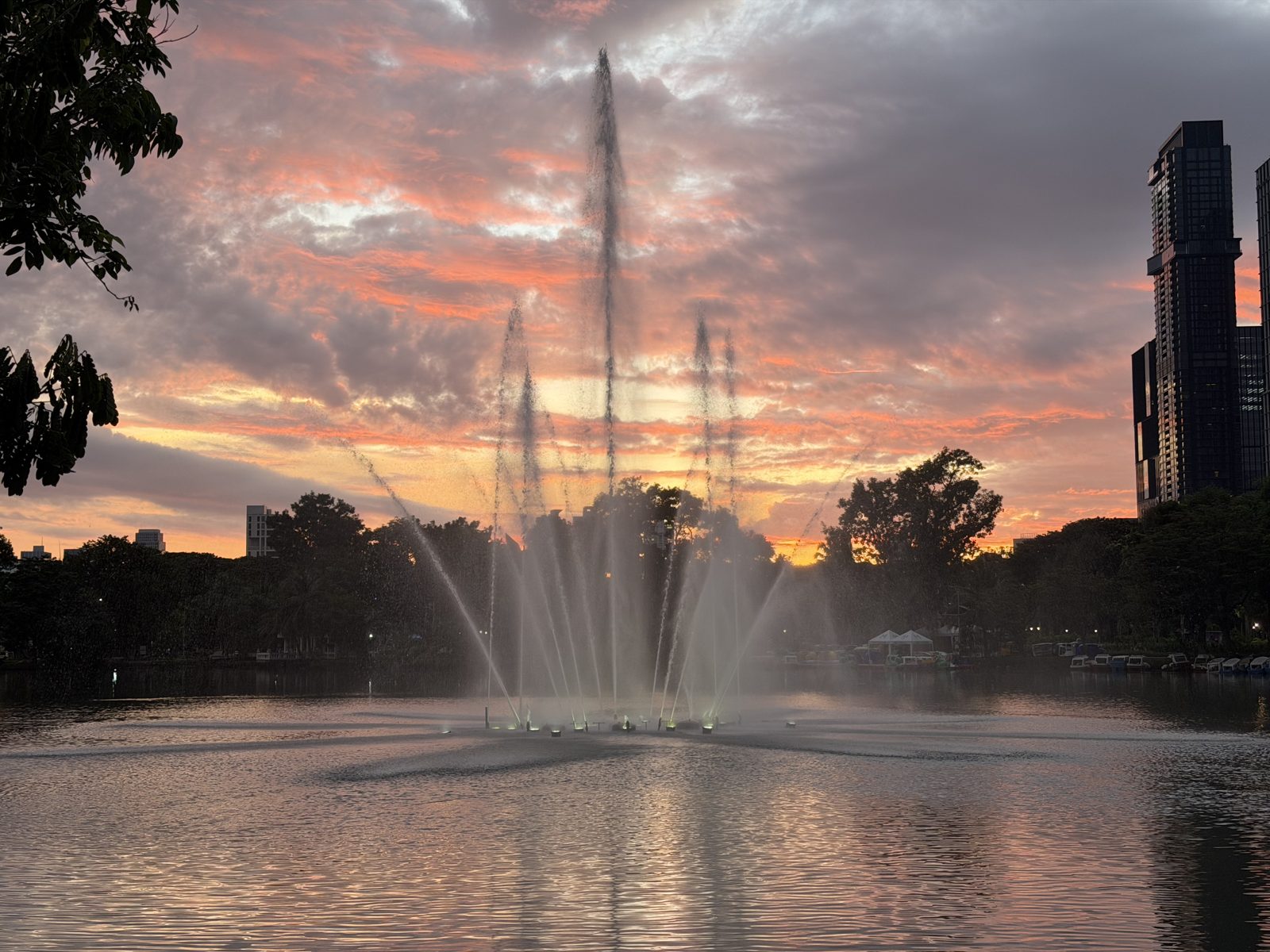 Pink sunrise and fountain across the lake at Lumphini Park in Bangkok